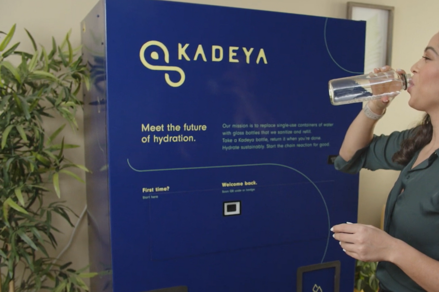 Woman drinking a bottle of water in front of a Kadeya sign